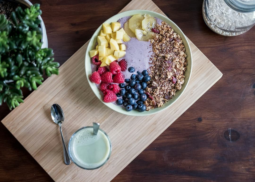 A bowl of fresh fruit, granola, and yogurt beside a glass of milk